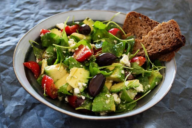 A plate consisting of olives, zucchini, tomatoes, and two slices of whole grain bread.