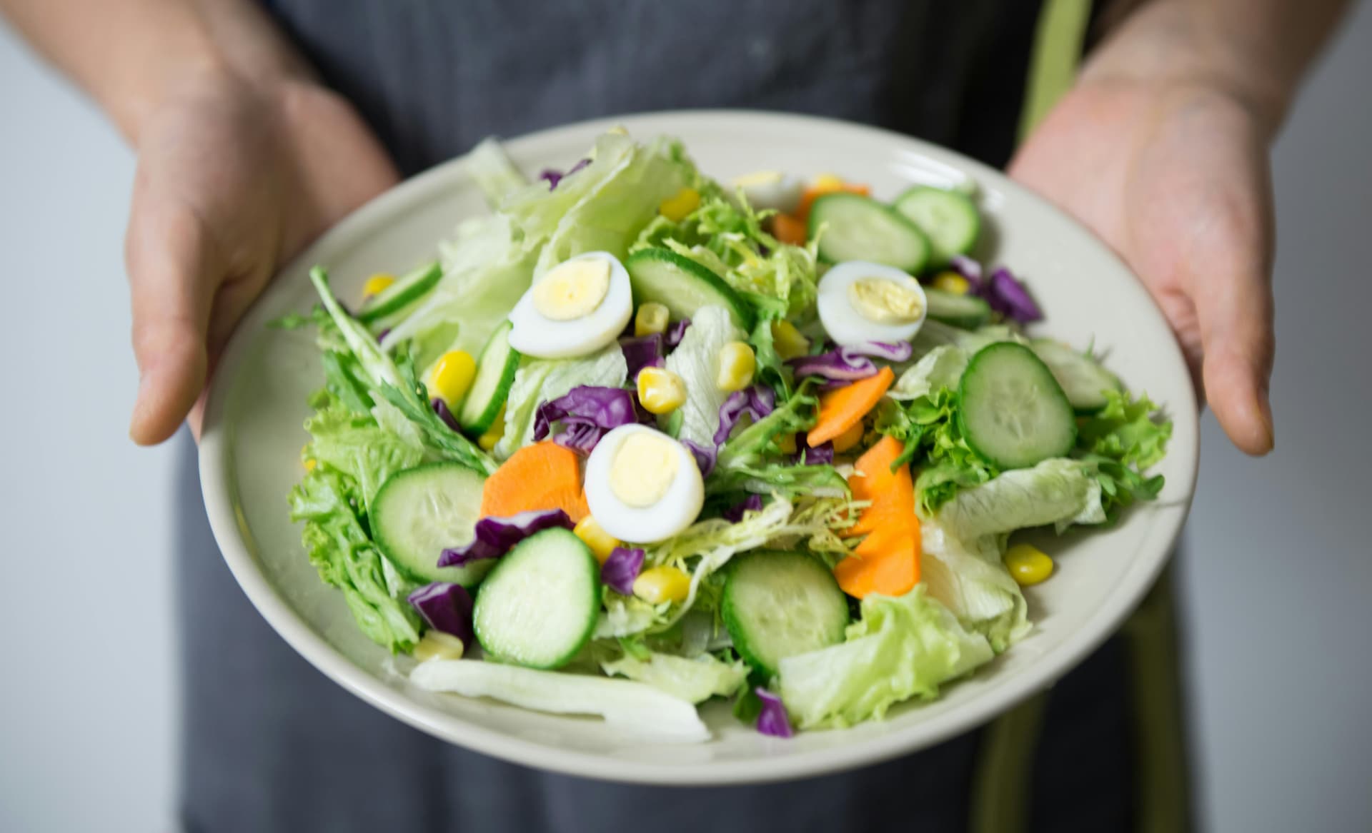 A dish consisting of cucumber, boiled egg, corn, carrot, and lettuce.