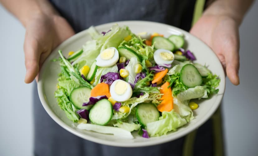 A dish consisting of cucumber, boiled egg, corn, carrot, and lettuce.