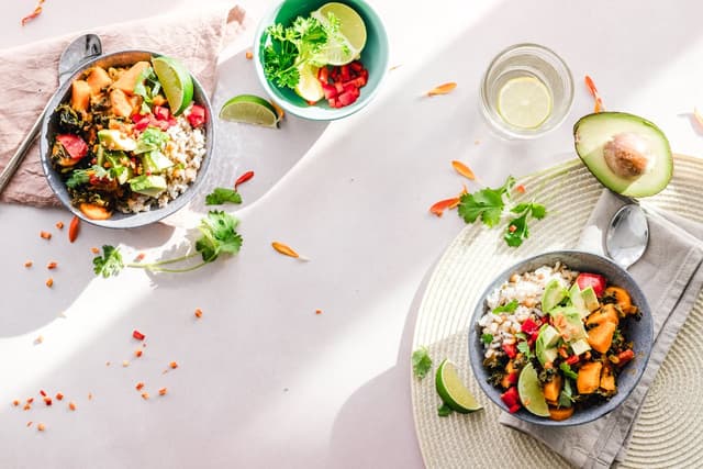 A healthy meal for two consisting of avocado, rice, lemon, and fruits.
